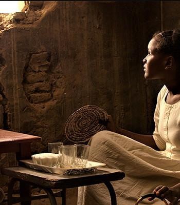 Afrikkalainen nuori tyttö istuu ja katsoo ikkunasta tulevaan valoon.