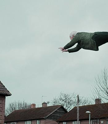 Ilmassa leijuva vanhus talojen yllä / An elderly man floating on top of houses