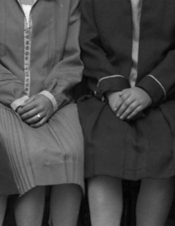 Neljä naista istuu kädet sylissä, päät ja jalat rajattu pois, mustavalkoinen kuva.