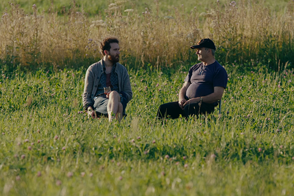 Kaksi miestä istuvat kesäisellä pellolla
