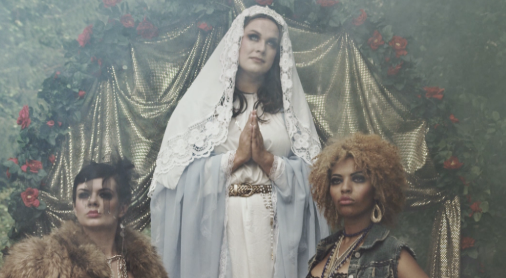 Kolme naista vierekkäin, joista keskimmäinen on pukeutunut Neitsyt Mariaksi. 