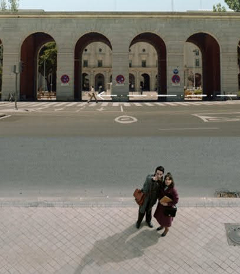 Mies ja nainen vierekkäin kadulla, mies osoittaa ylös kohti kameraa.