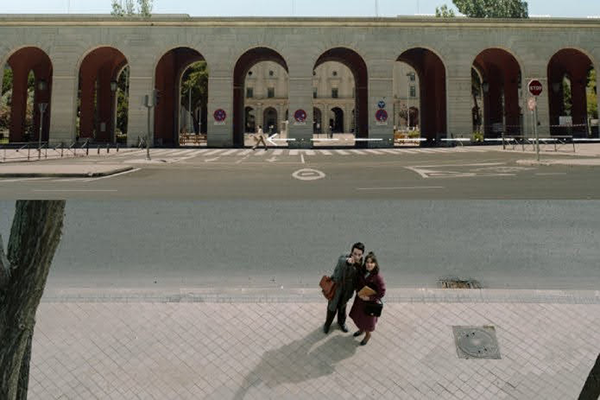 Mies ja nainen vierekkäin kadulla, mies osoittaa ylös kohti kameraa.
