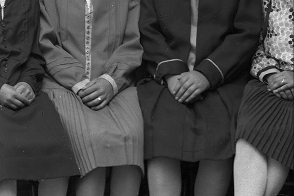 Mustavalkoinen kuva neljästä vierekkäin istuvasta naisesta. Naisilla on samanlaiset vekkihameet ja jokainen pitää käsiään sylissään.