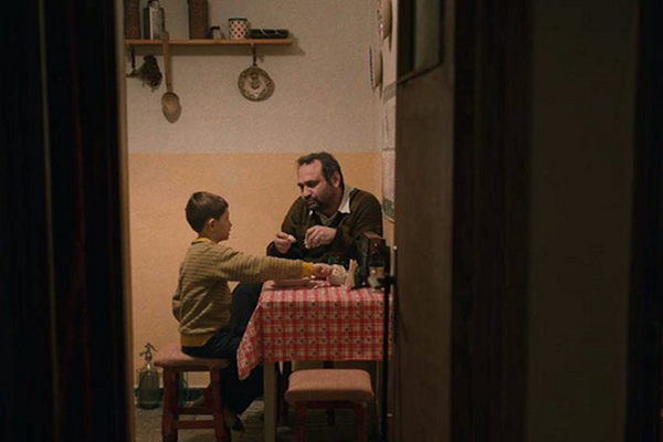 Poika ja isä istuvat keittiöpöydän äärellä.