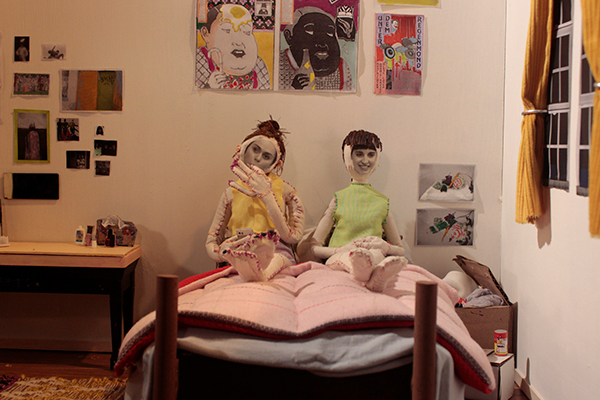Miniatyyrisängyssä makaa kaksi nukkea, joiden kasvoille on liimattu valokuvat kasvoista.