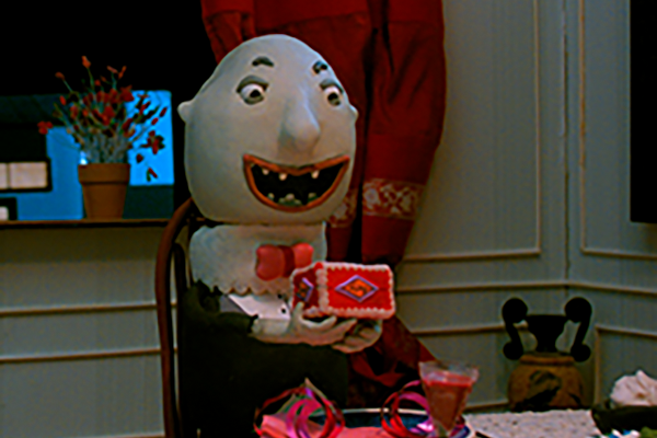 Vaha-animoitu kuva, jossa kalpea vampyyrimäinen hahmo istuu pöydän päässä ja pitelee käsissään rasiaa leveästi hymyillen.