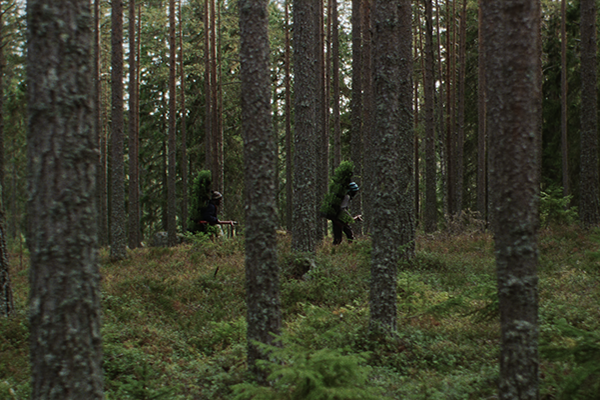 Kaksi hahmoa kävelee suuret rinkat selässään metsän läpi.