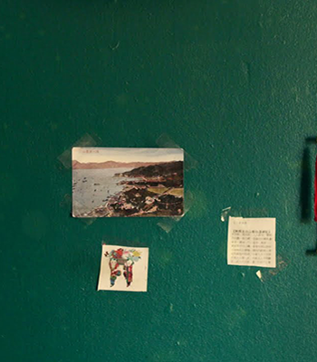 Vihreä seinä, johon on teipattu kuvia, muistilappu ja punainen koriste-esine.