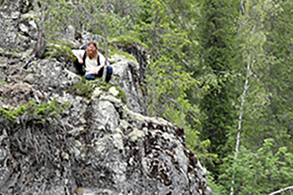 Rakeinen kuva miehestä, joka istuu kalliolla vihreän metsän keskellä.
