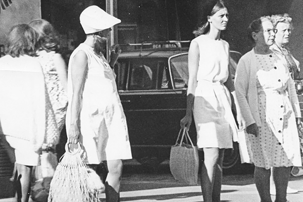 Mustavalkokuva, jossa retrohenkisiin vaatteisiin pukeutuneet naiset seisovat kadulla.