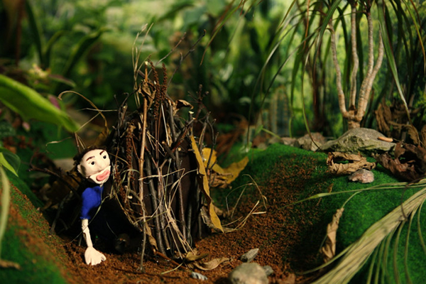 Stop motion -animaatiomaisema metsästä, jossa hahmo kurkkaa ulos risumajasta.