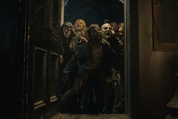 Avoin ulko-ovi, jonka kynnyksen yli puskee zombeja.