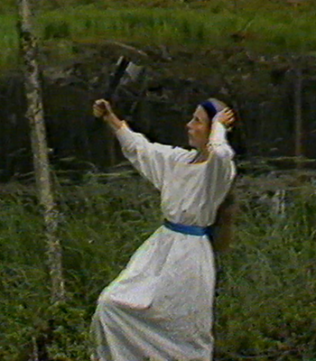 Suomi-neito seisoo ruohoisella suolla vasara kädessään.