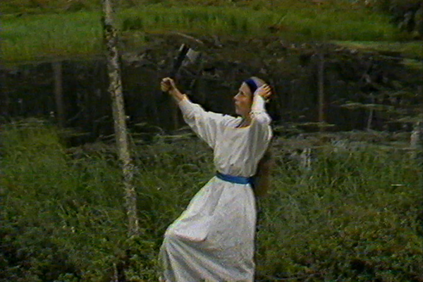 Suomi-neito seisoo ruohoisella suolla vasara kädessään.